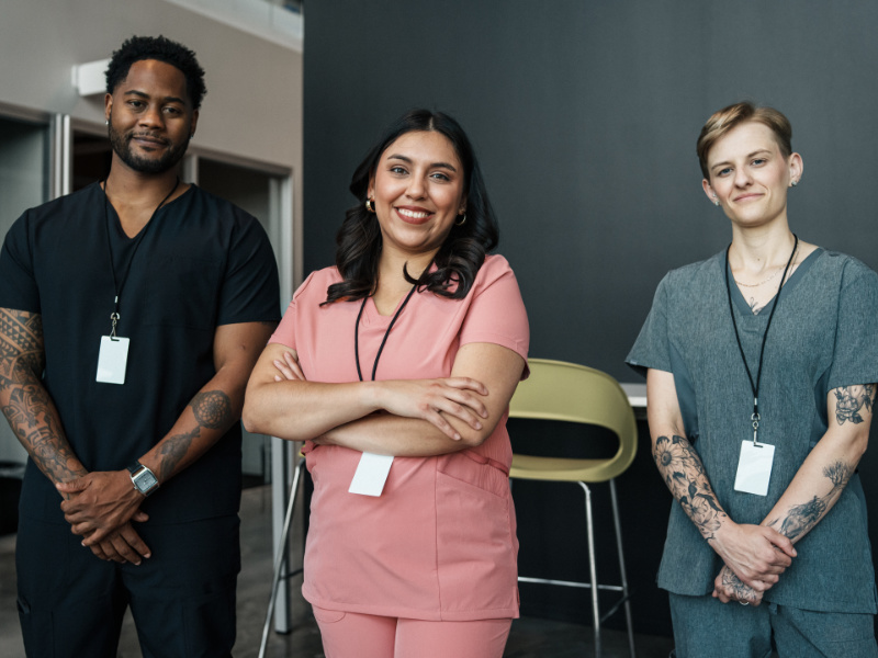 Portrait of a multiracial group of nurses wearing medical scrubs standing together in a hospital corridor and smiling directly at the camera.